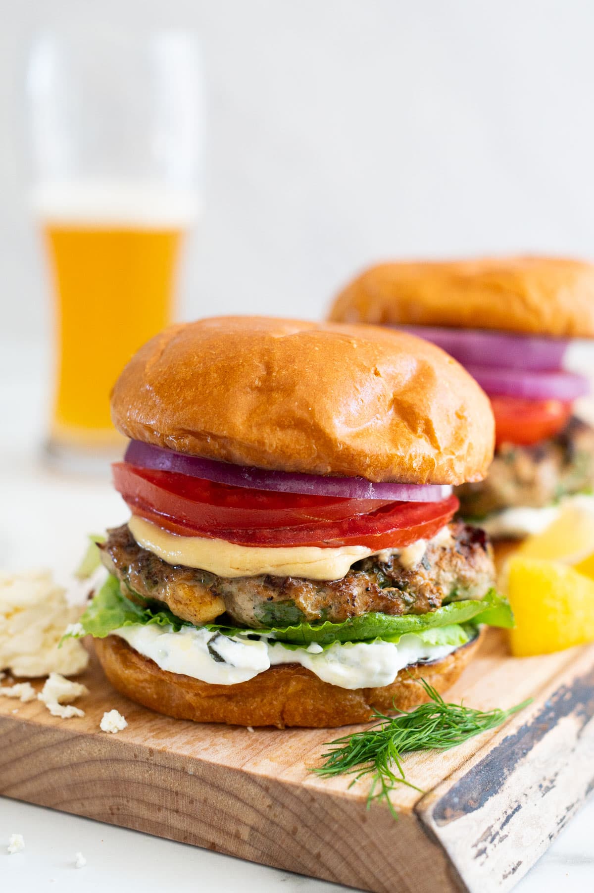 Spinach feta turkey burgers served on a wooden board with beer in a glass in a background.