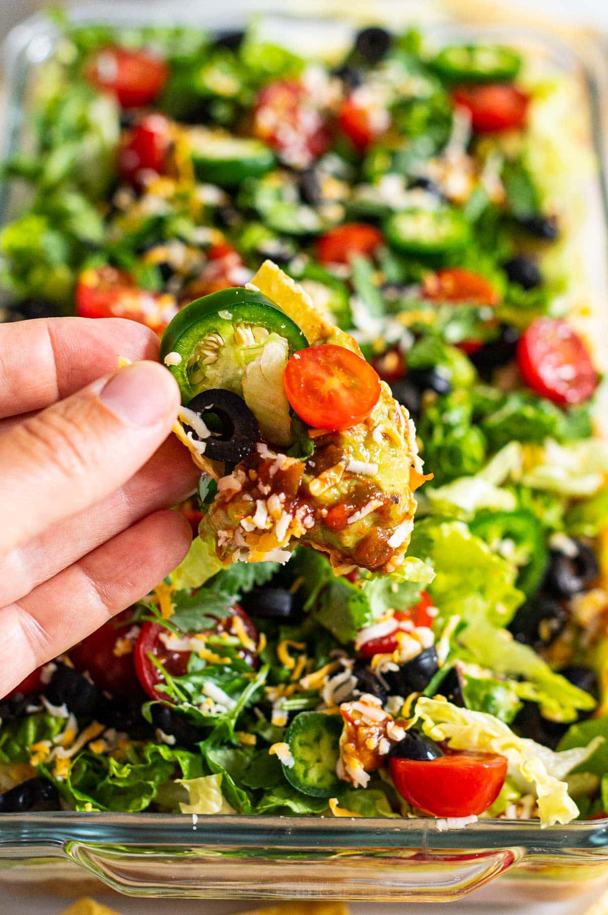 Person holding tortilla chip scooped up with healthy seven layer dip.