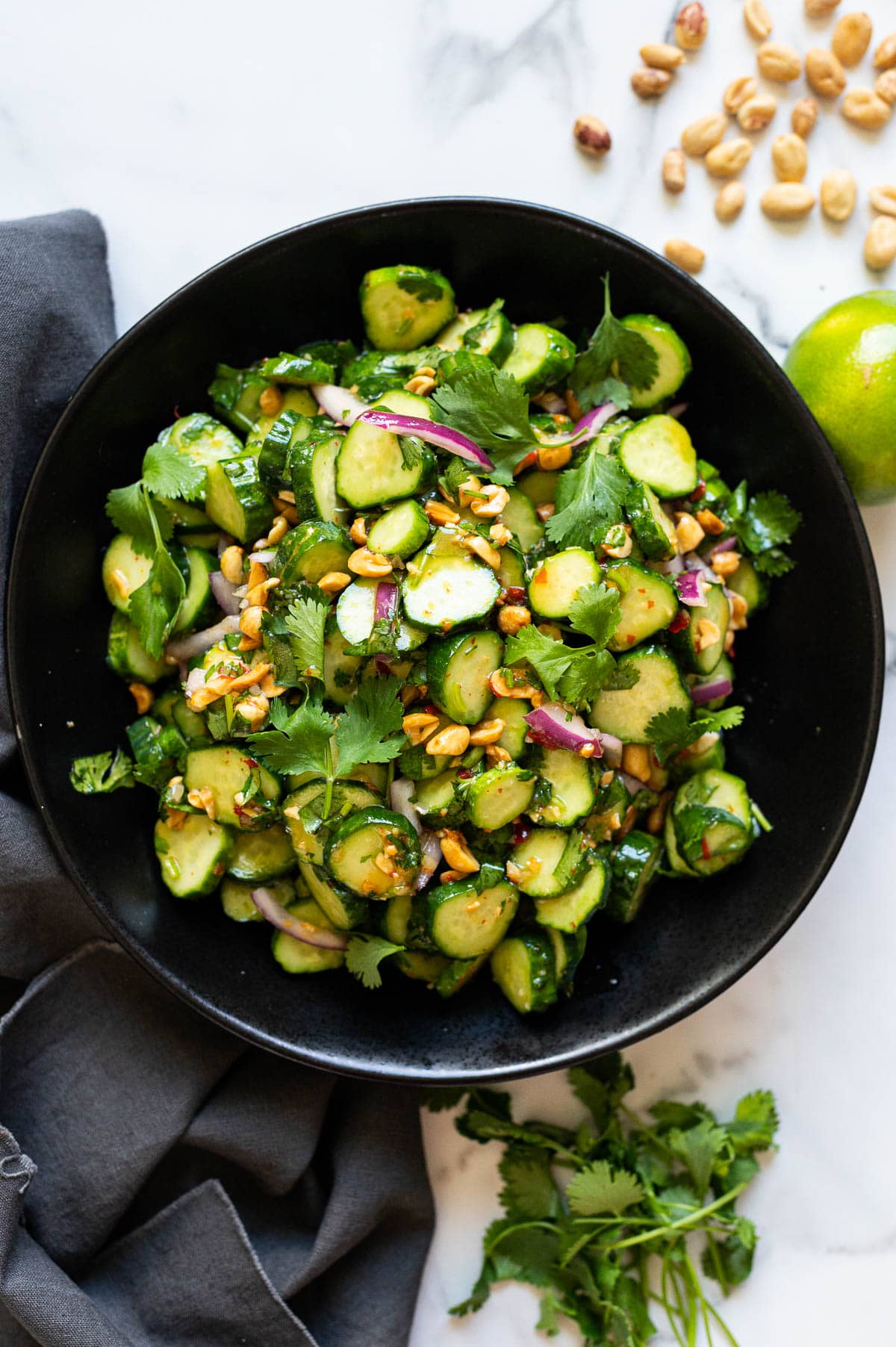 Thai cucumber salad served in black bowl. Gray napkin, lime and peanuts on a countertop.