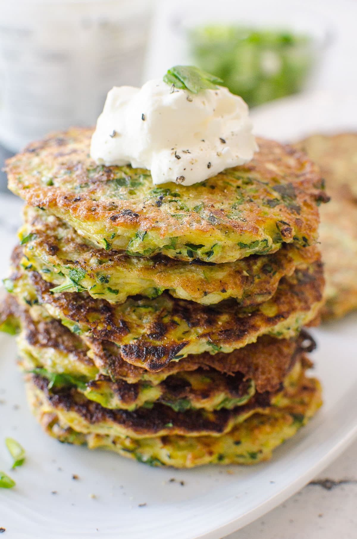 Baked zucchini fritters stacked with dollop of sour cream on top on 
a plate.