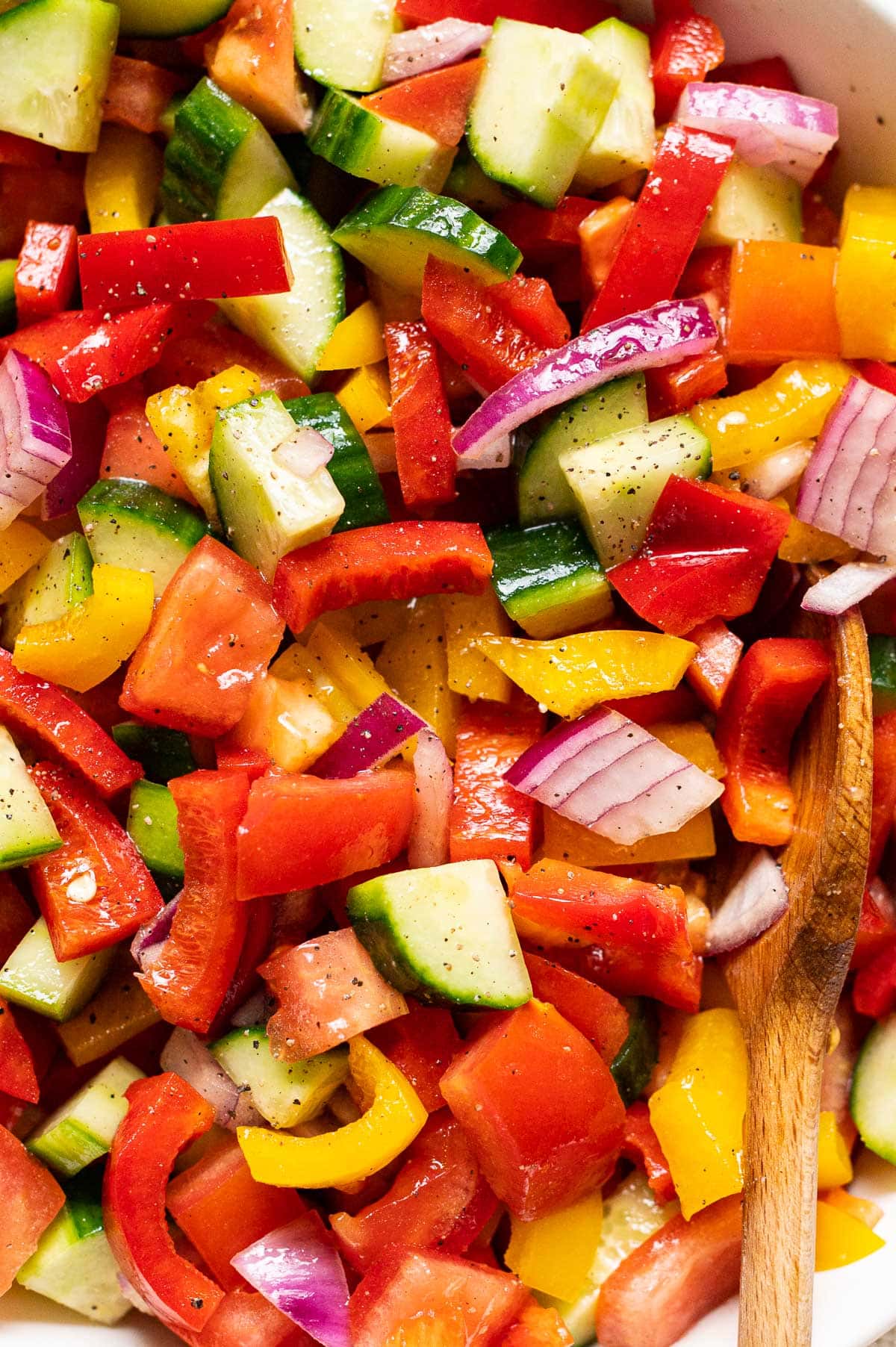 Closeup of bell pepper salad seasoned with ground black pepper and wooden spoon in it.