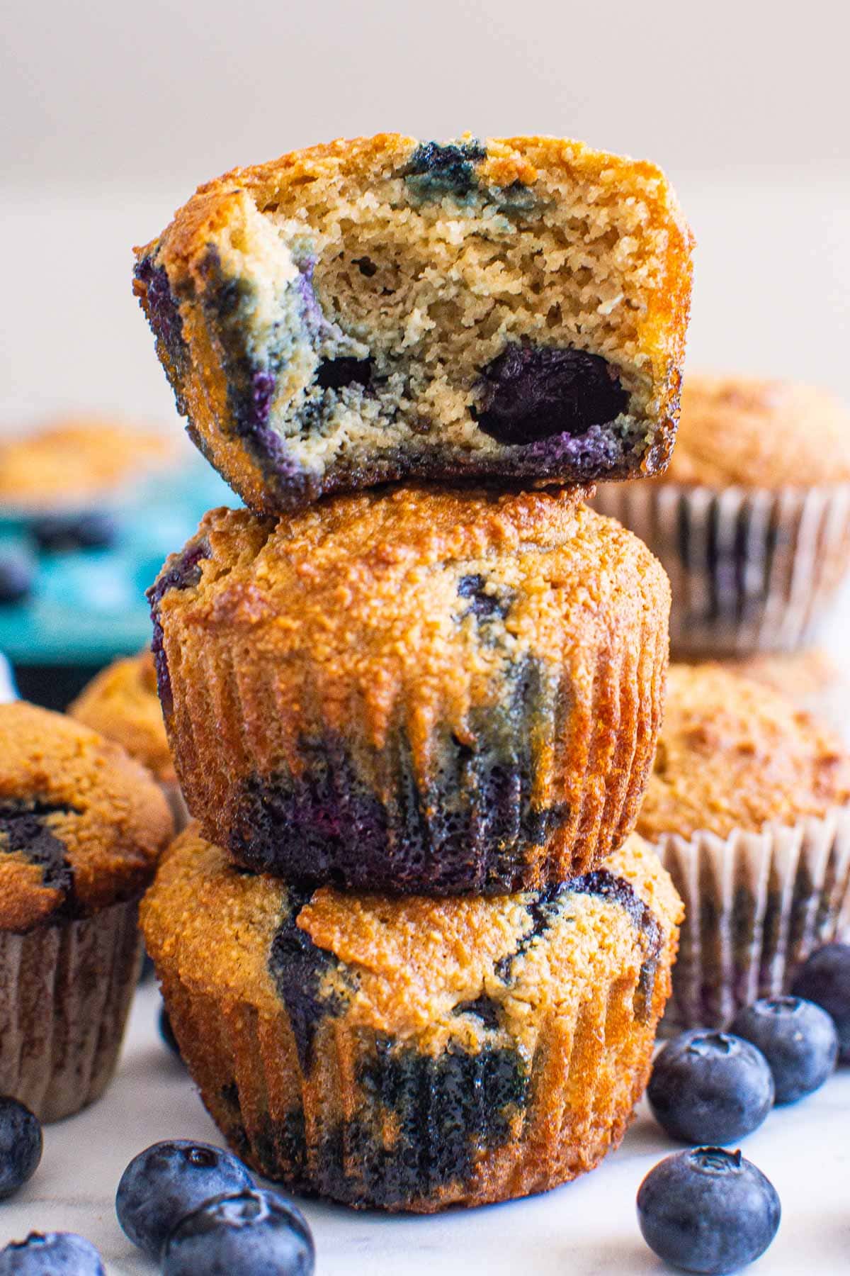 Three stacked almond flour blueberry muffins and top one showing texture inside.