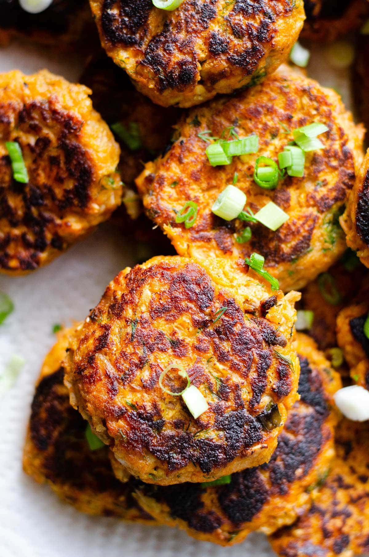 Close up of canned salmon cakes stacked on a platter. Garnished with dill and green onion.