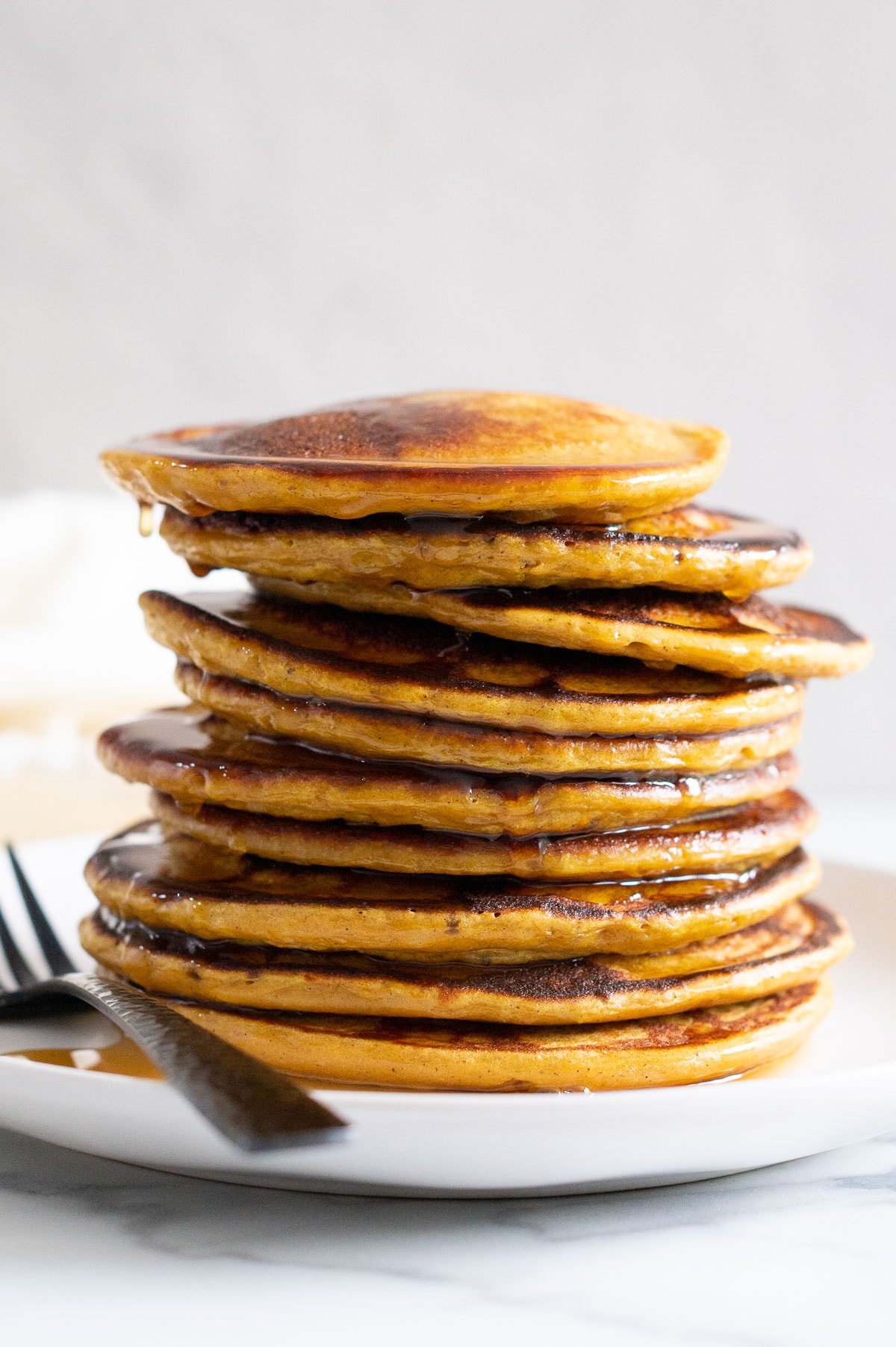 A stack of cottage cheese protein pancakes drizzled with maple syrup and served on a plate with a fork.