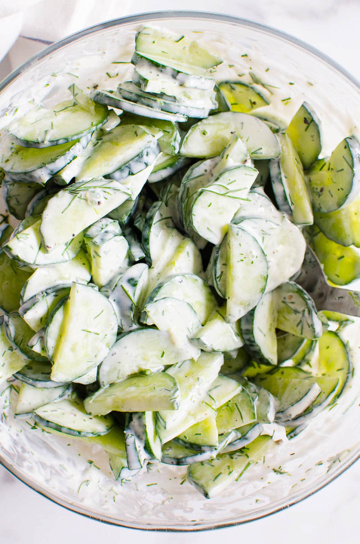 Creamy cucumber salad in glass bowl with metal spoon.