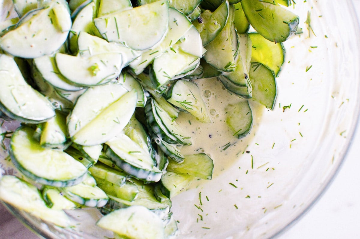 Cucumber salad in a bowl with lots of liquid at the bottom of the bowl.