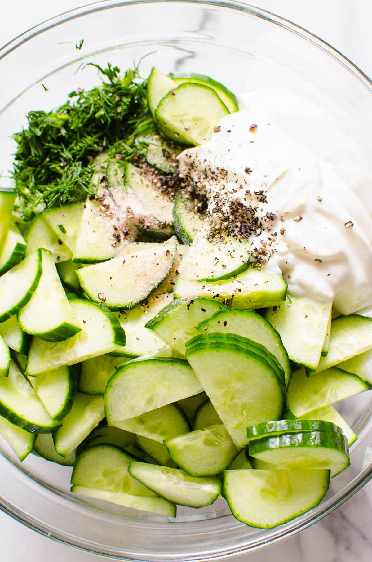 Sliced cucumbers, chopped dill, yogurt, salt and pepper in a bowl.