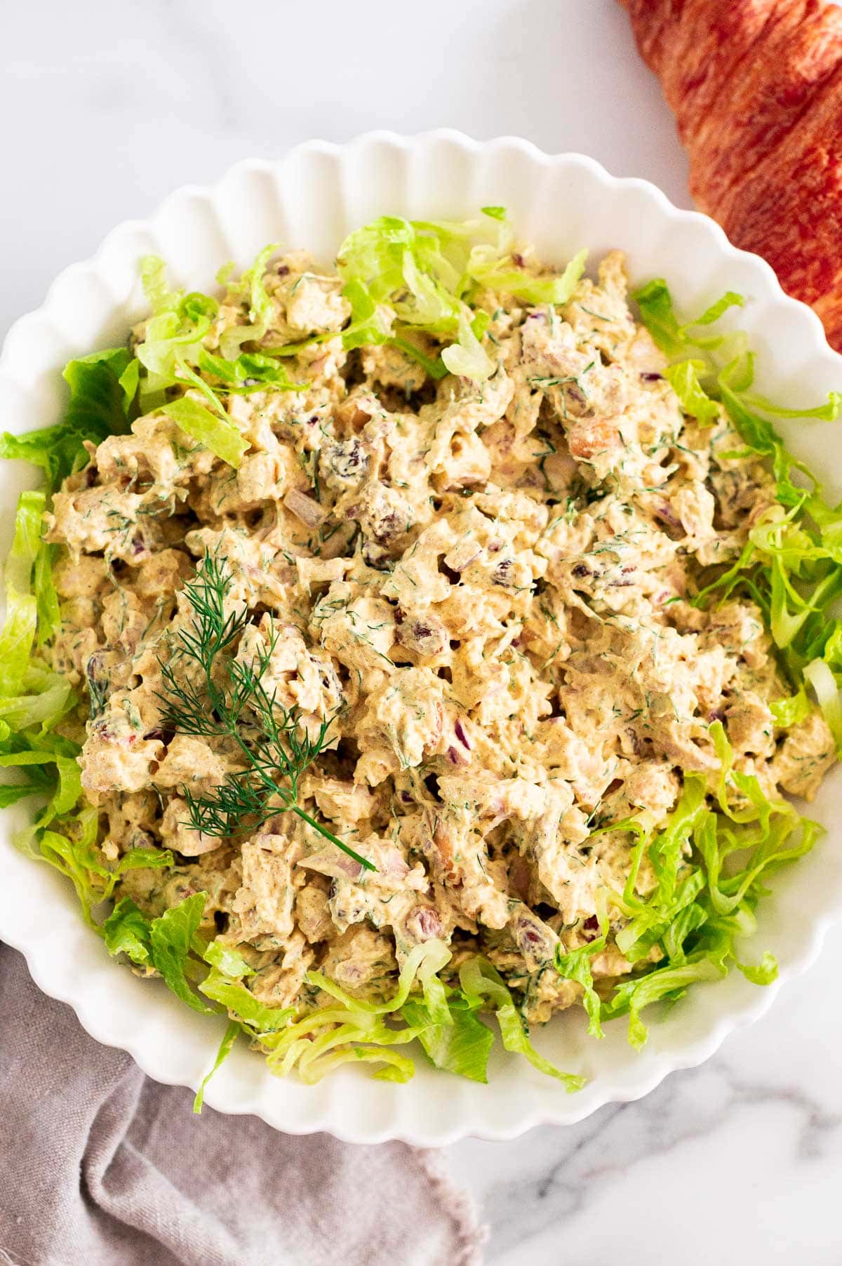 Curry chicken salad served in a bowl with lettuce and garnished with dill.