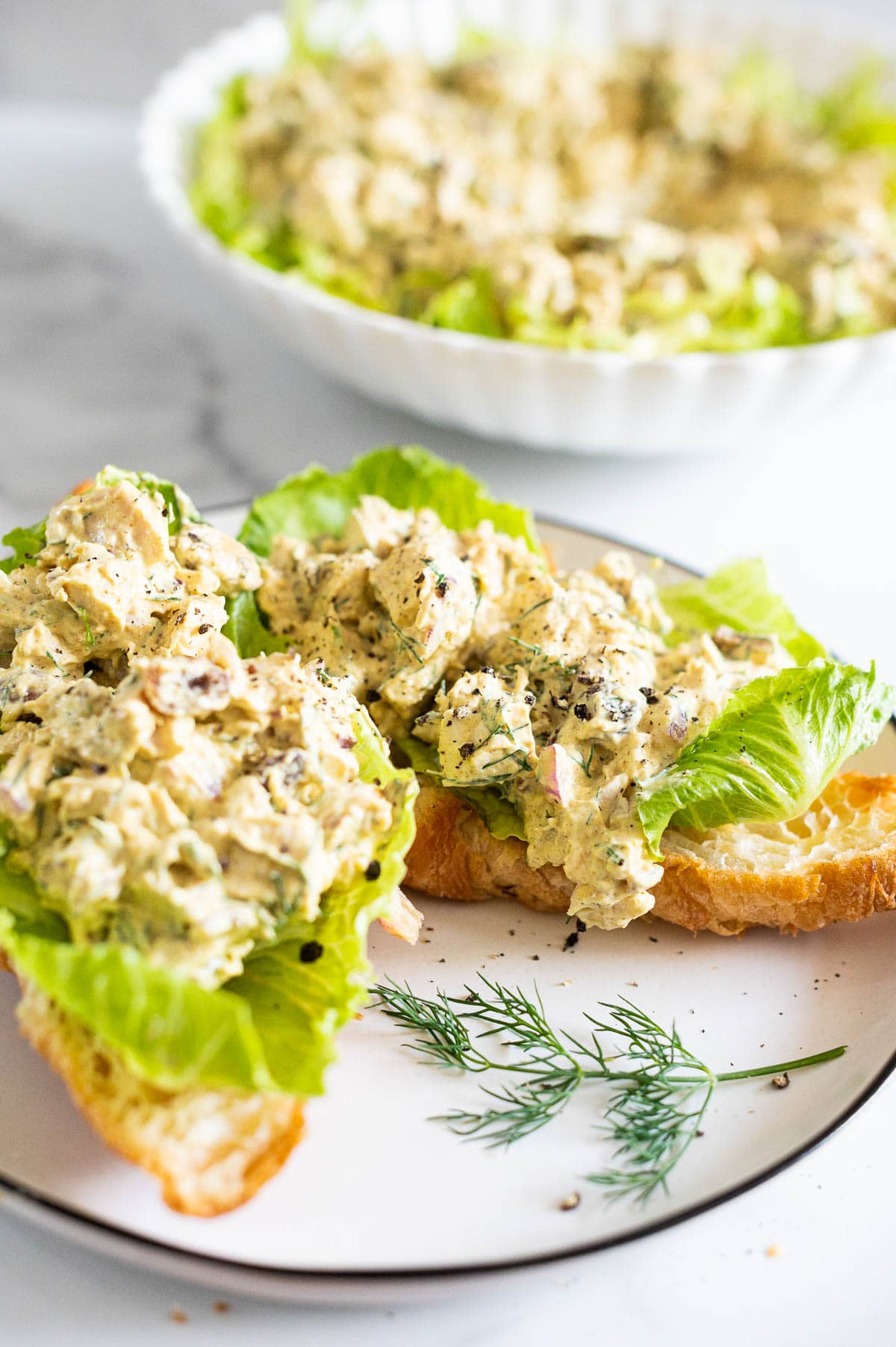 Curry chicken salad served on a croissant with lettuce on a plate.