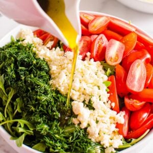 Arugula feta salad with tomatoes and dill drizzled with balsamic dressing in a bowl.