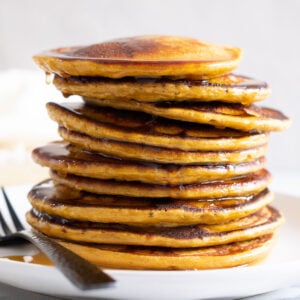 A stack of cottage cheese protein pancakes drizzled with maple syrup and served on a plate with a fork.