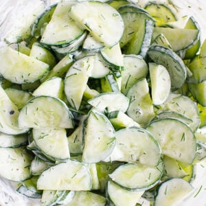 Creamy cucumber salad in glass bowl with metal spoon.