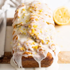 Lemon zucchini bread with icing and lemon zest on top served on a platter. Knife, linen napkin and lemon.