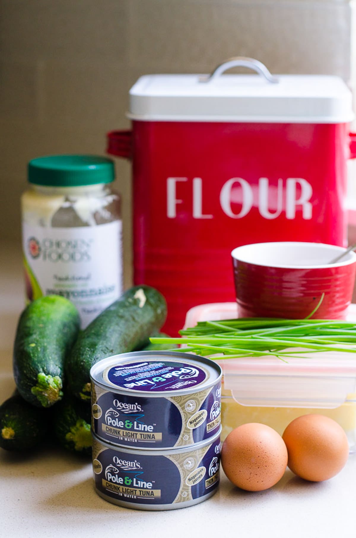 Canned tuna, eggs, chives, zucchini, cheese in container, salt in a bowl, mayo, and flour tin.