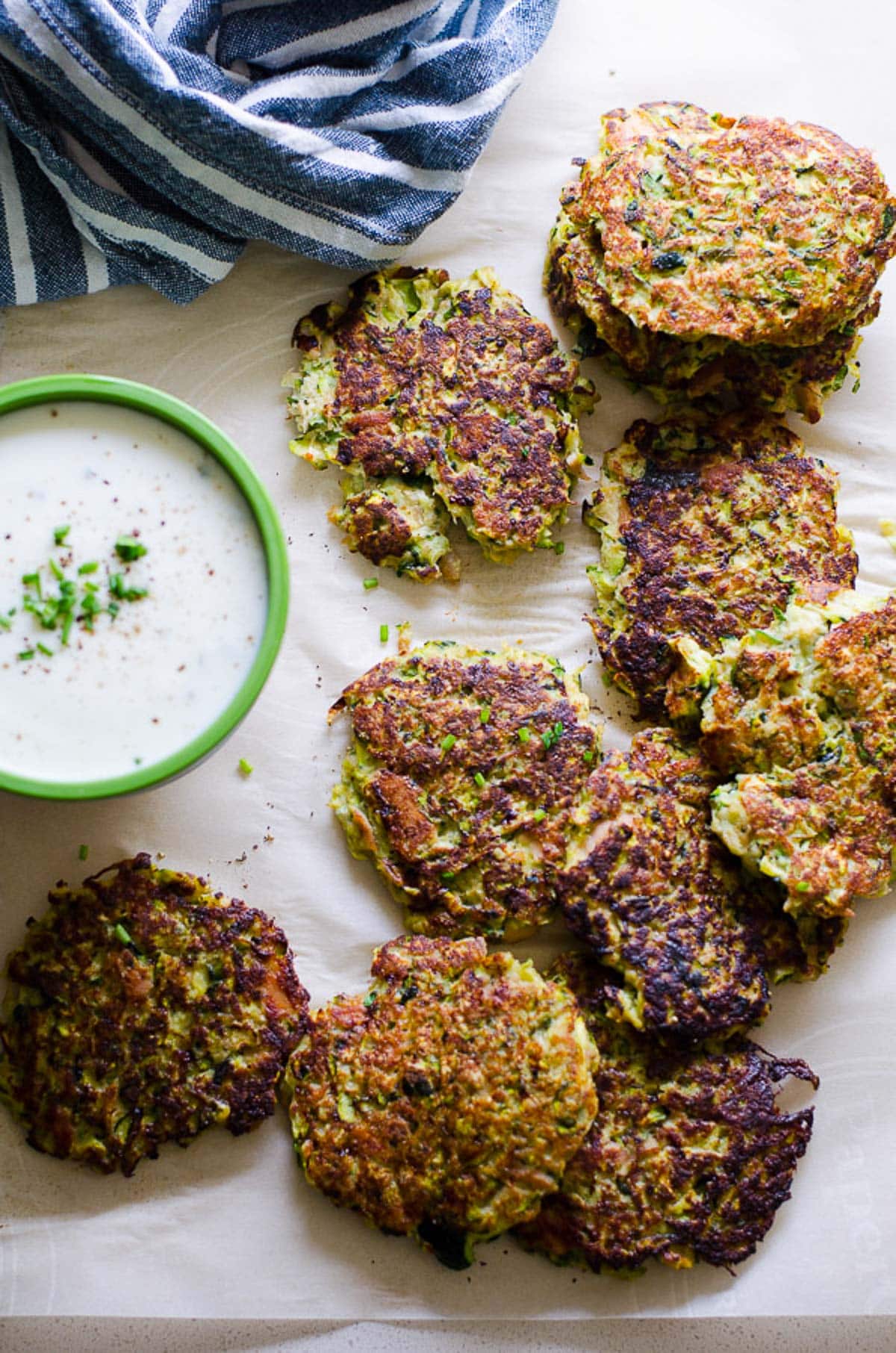Fried zucchini cakes served with creamy dipping sauce and garnished with chives.
