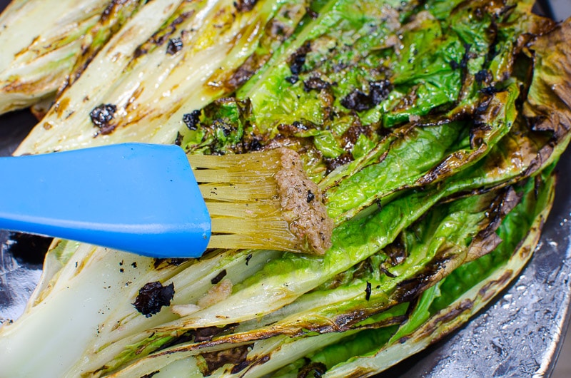Brushing grilled romaine lettuce heart with garlic anchovy sauce.
