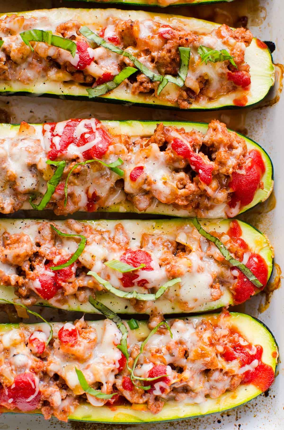 Ground turkey zucchini boats garnished with basil in a baking dish.