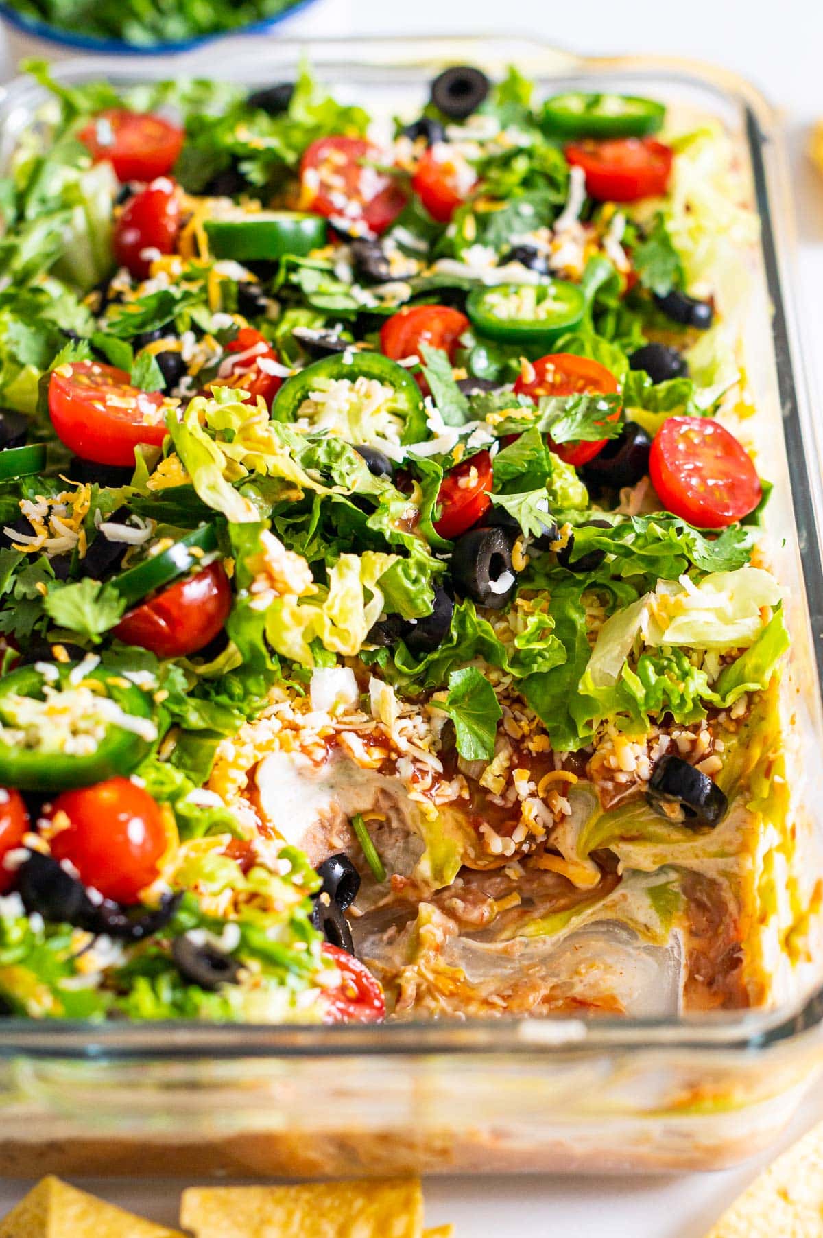 Healthy seven layer dip garnished with jalapenos and olives and served in a baking dish showing texture inside.
