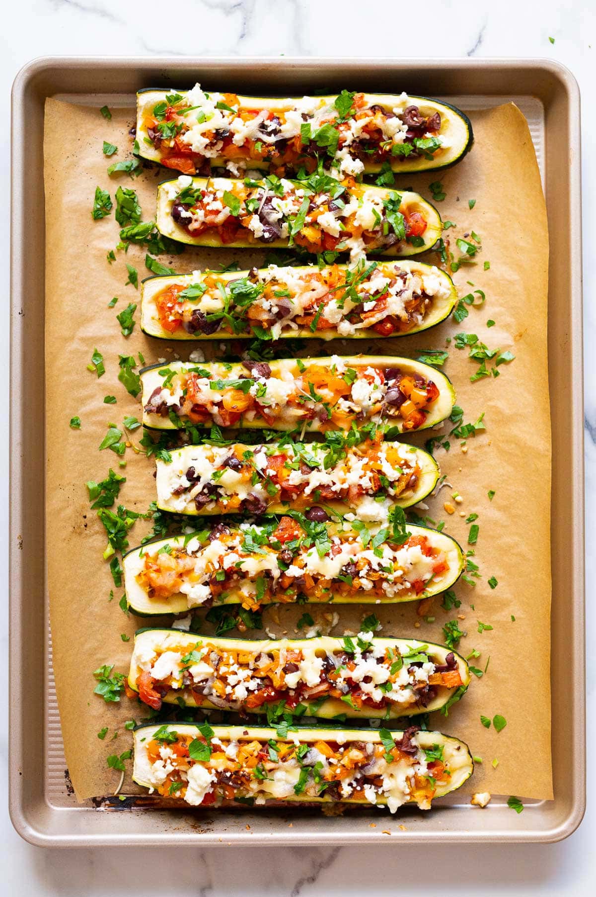 Mediterranean zucchini boats on baking sheet lined with parchment paper.