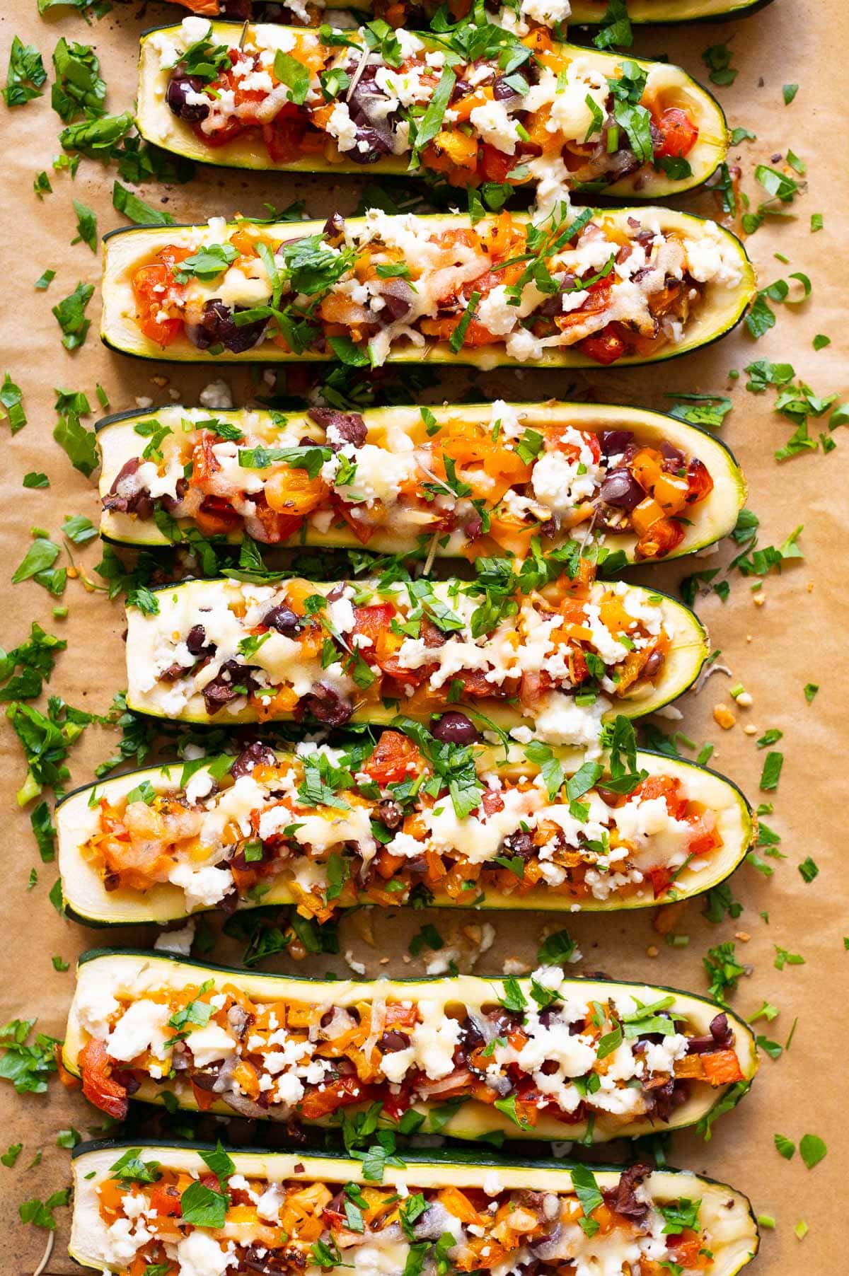 Mediterranean zucchini boats garnished with parsley on parchment paper lined tray.