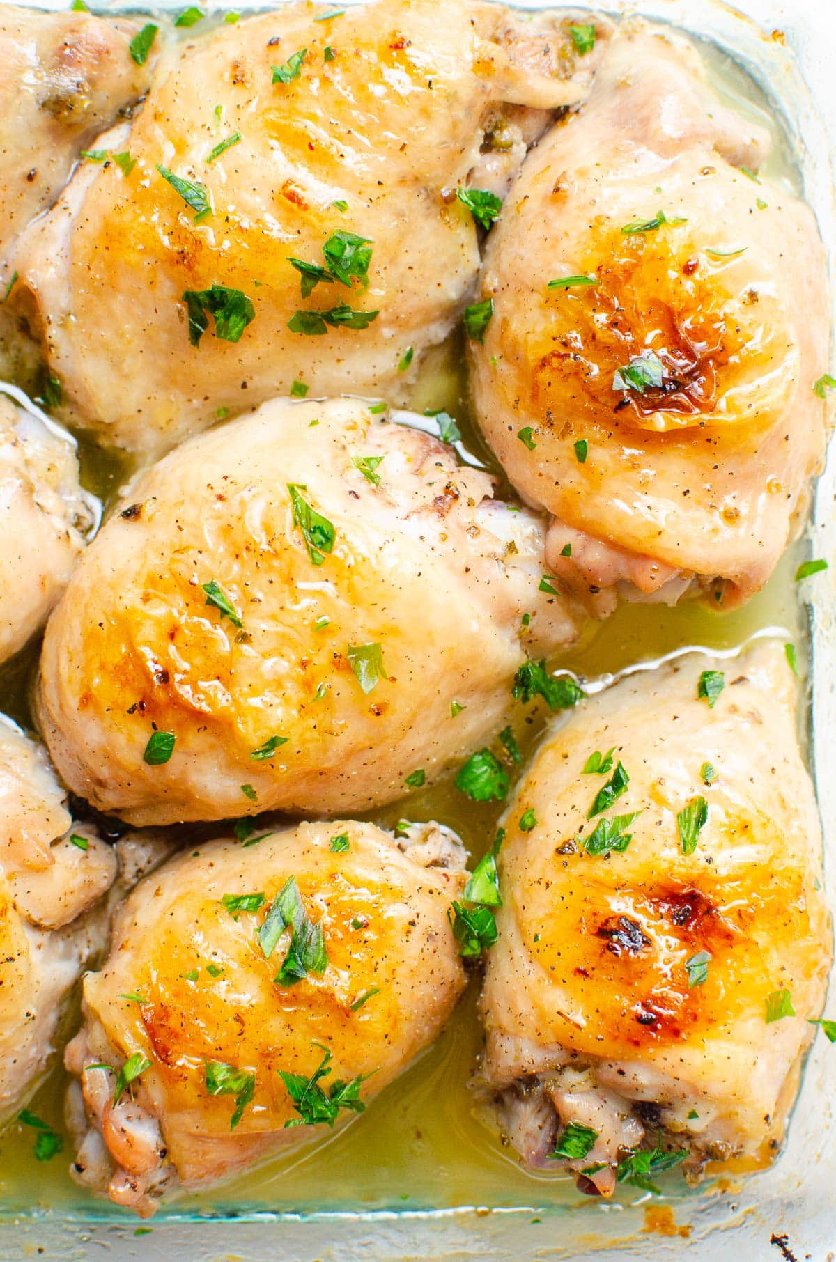 Oven baked chicken thighs with crispy skin and garnished with parsley in a baking dish.