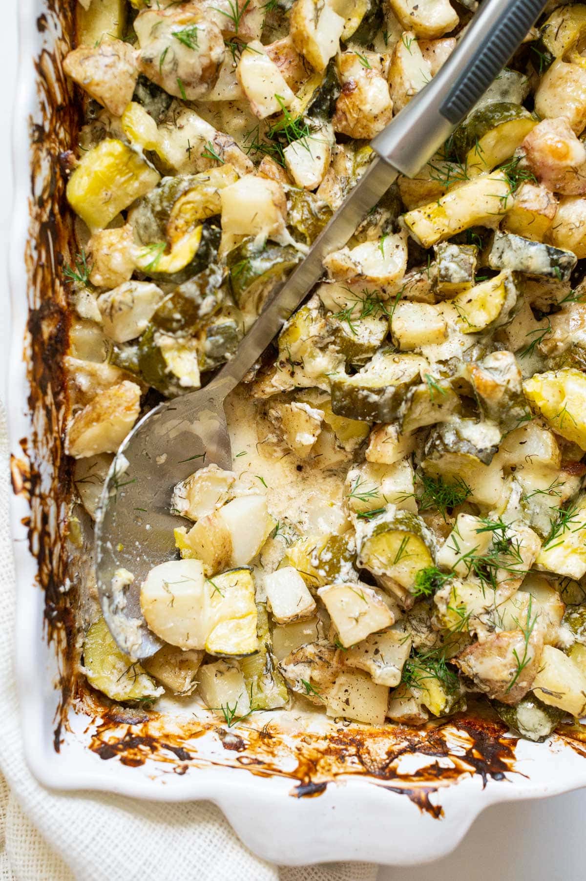 Zucchini potato casserole showing texture in a baking dish with a metal spoon.