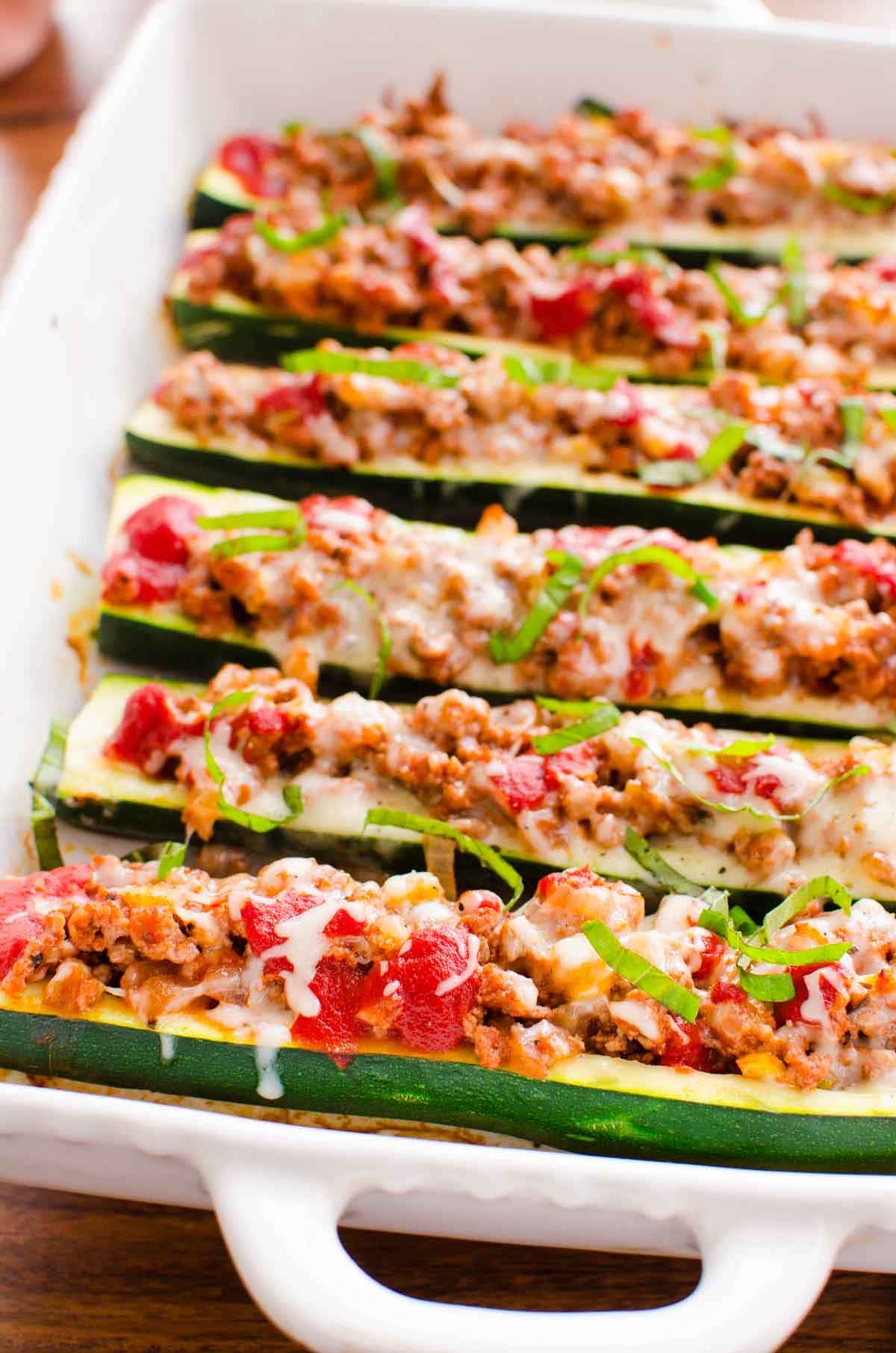 Side view of ground turkey zucchini boats with melted cheese and fresh basil on top.