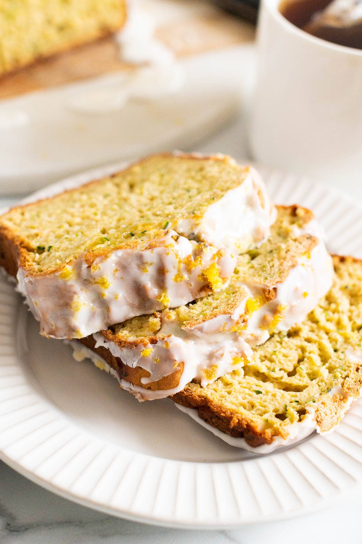 Three slices of zucchini lemon bread with icing on a plate.