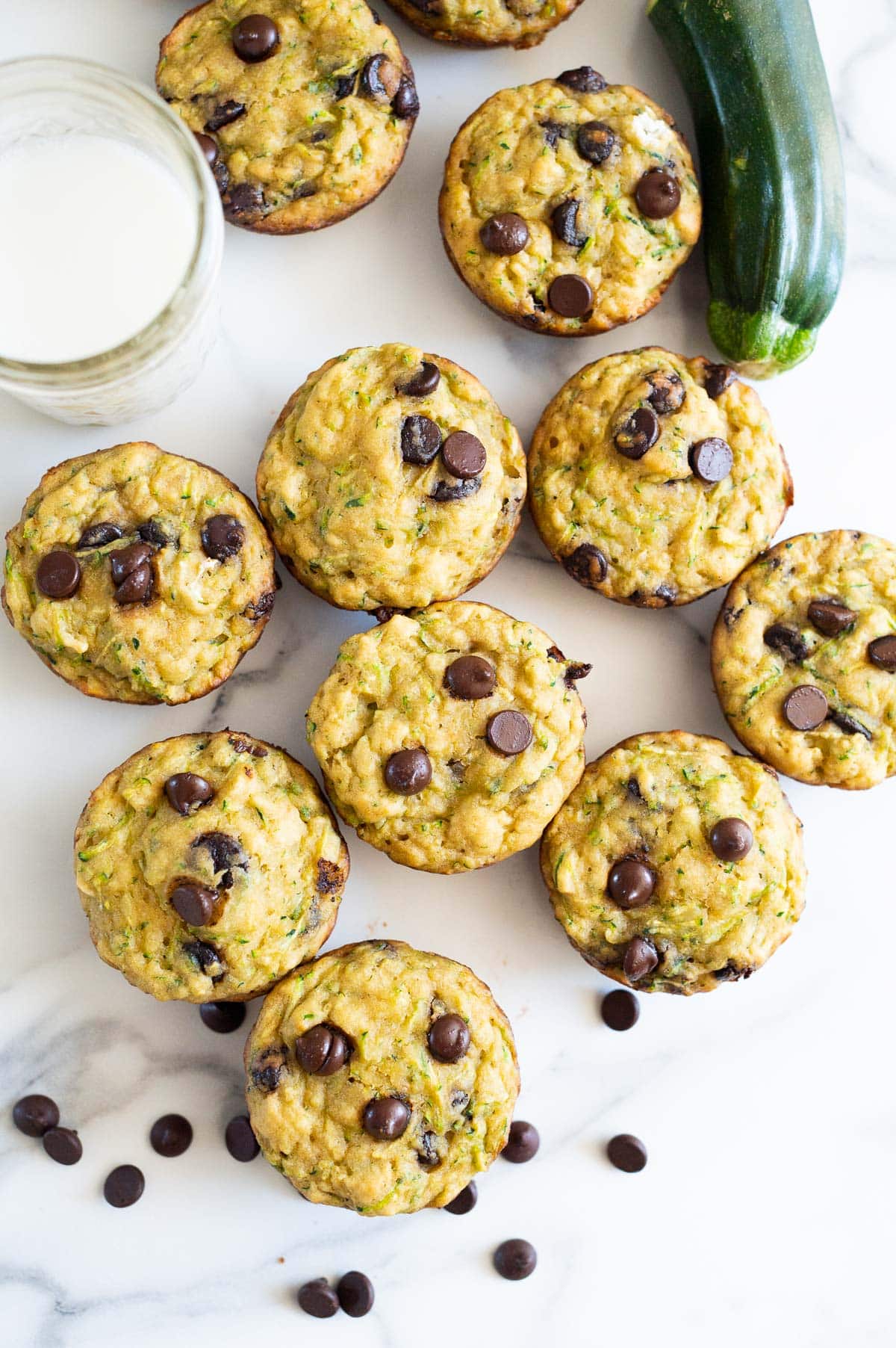 Looking down on zucchini chocolate chip muffins, glass of milk and zucchini.