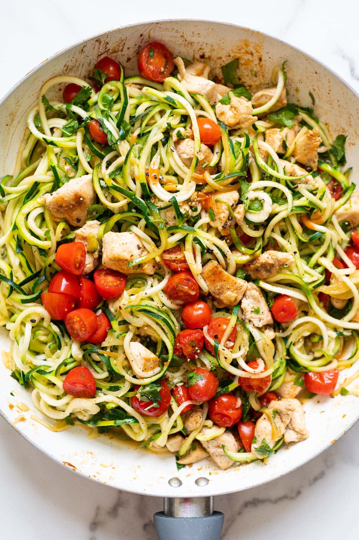 Zucchini noodles with chicken, grape tomatoes and cilantro in white skillet.
