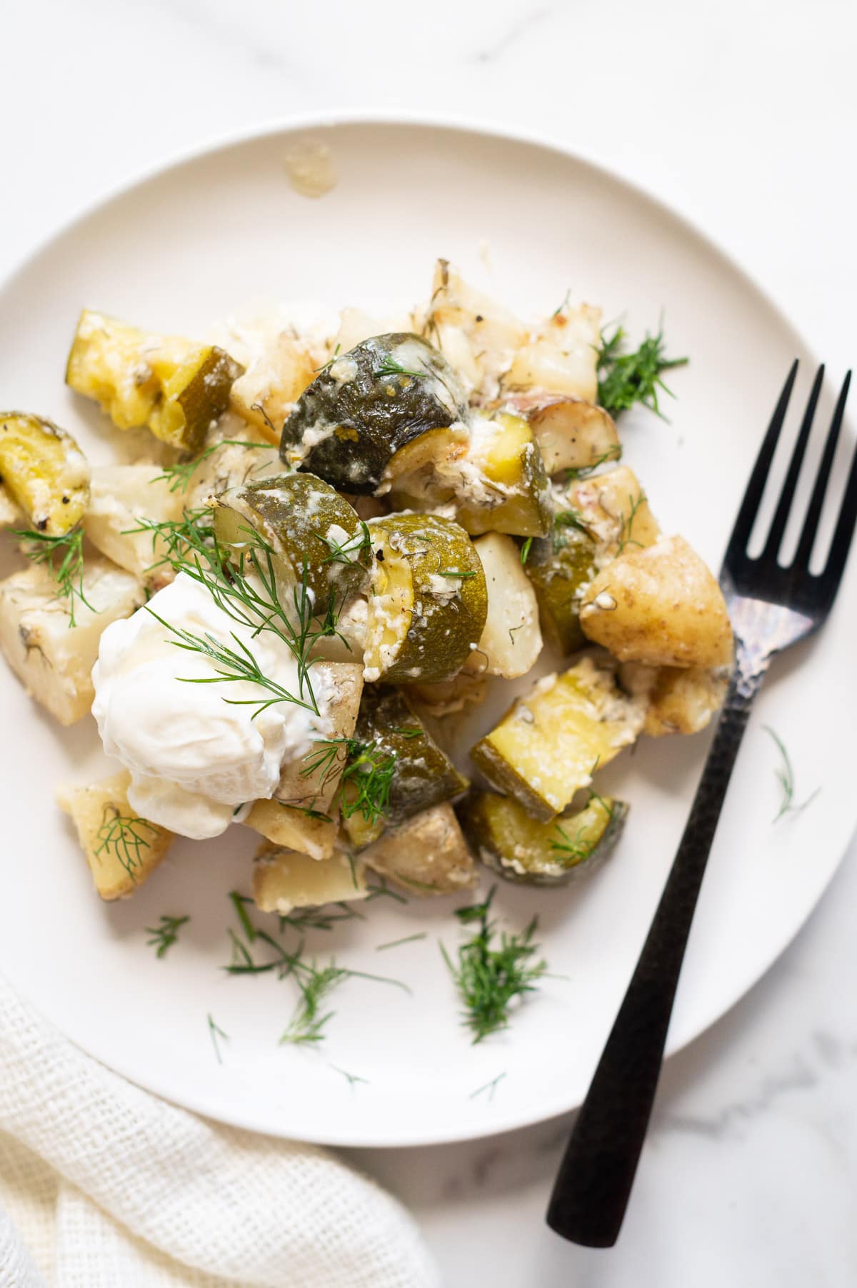 Zucchini potato casserole served with a dollop of sour cream and fresh dill on a plate with a fork.