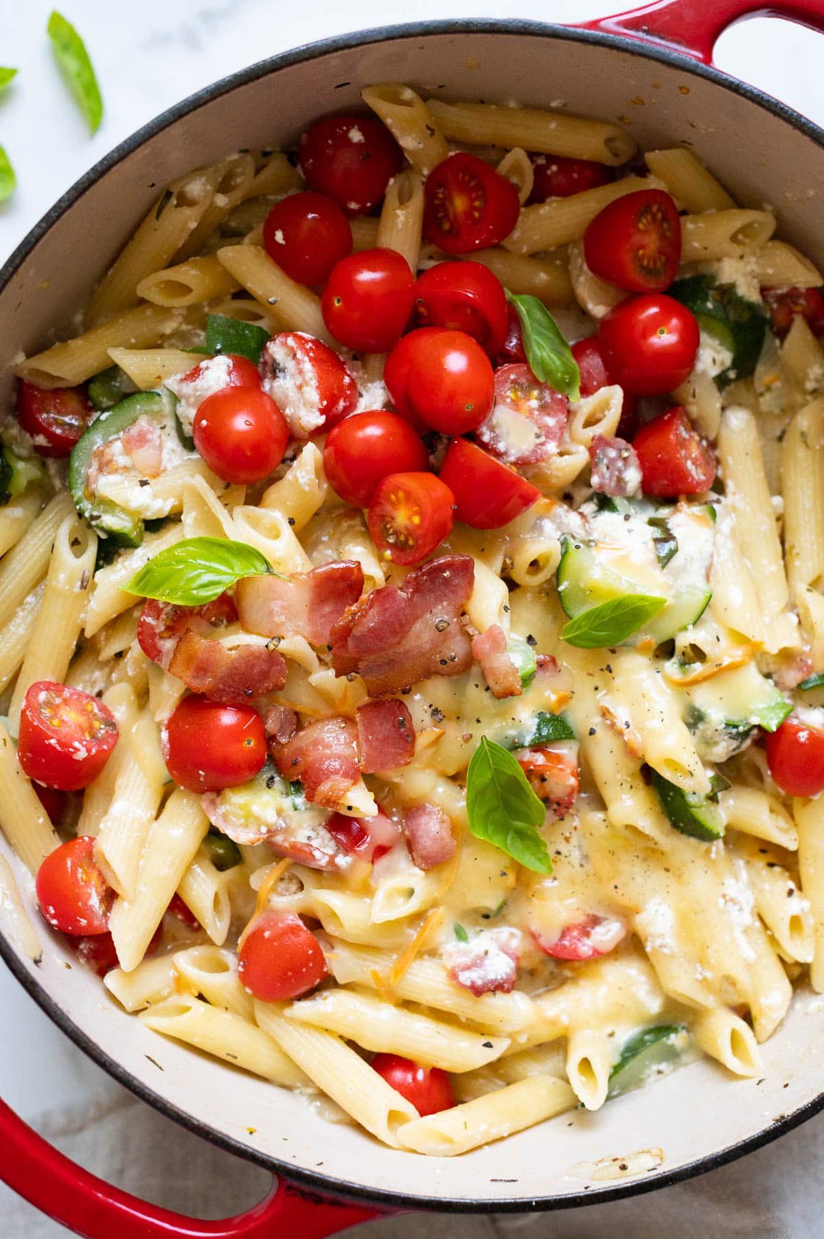 Zucchini ricotta pasta with tomatoes, bacon and cheese in a red pot.