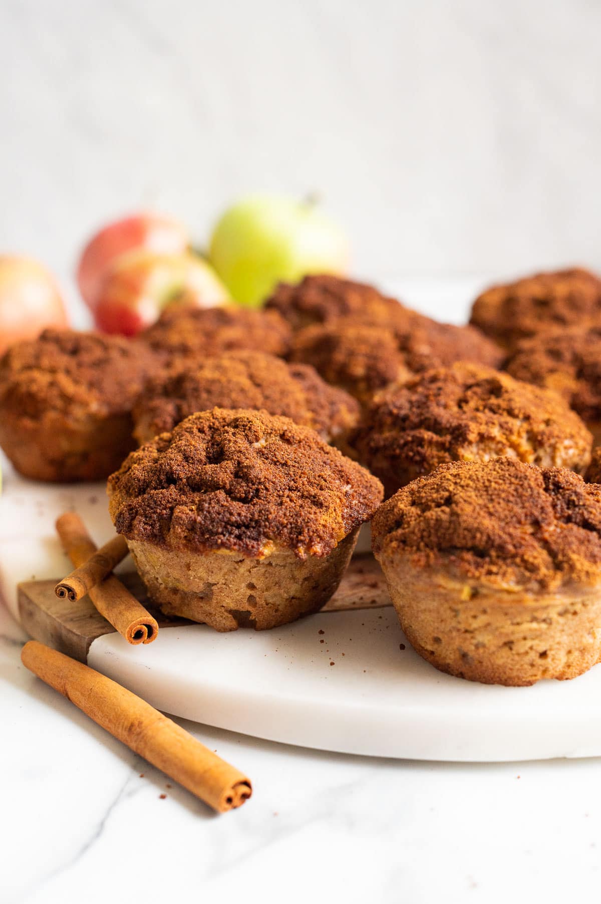 Apple cinnamon muffins on a platter. Cinnamon sticks and apples in the background.