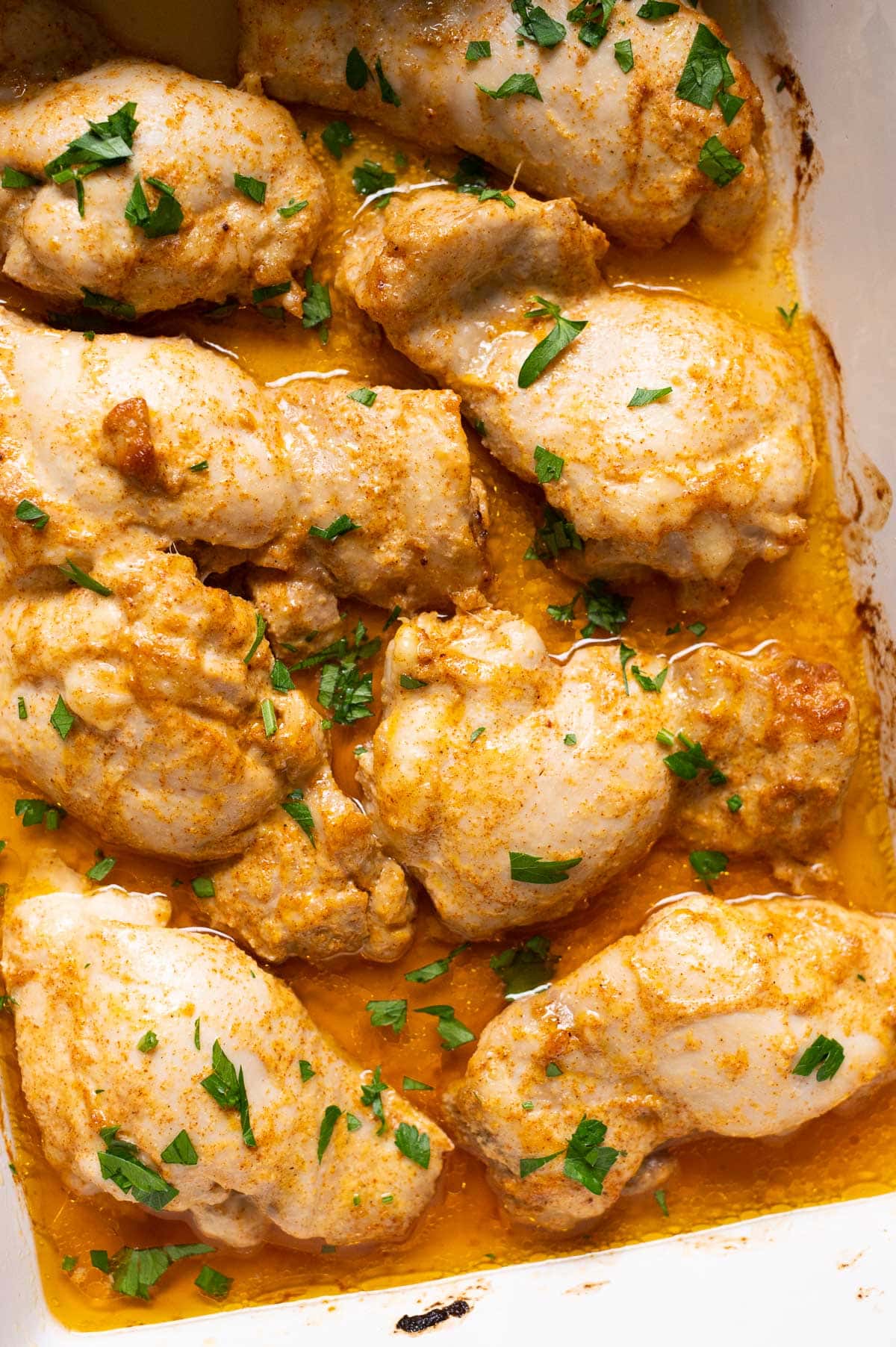 Baked boneless chicken thighs garnished with parsley in a baking dish.