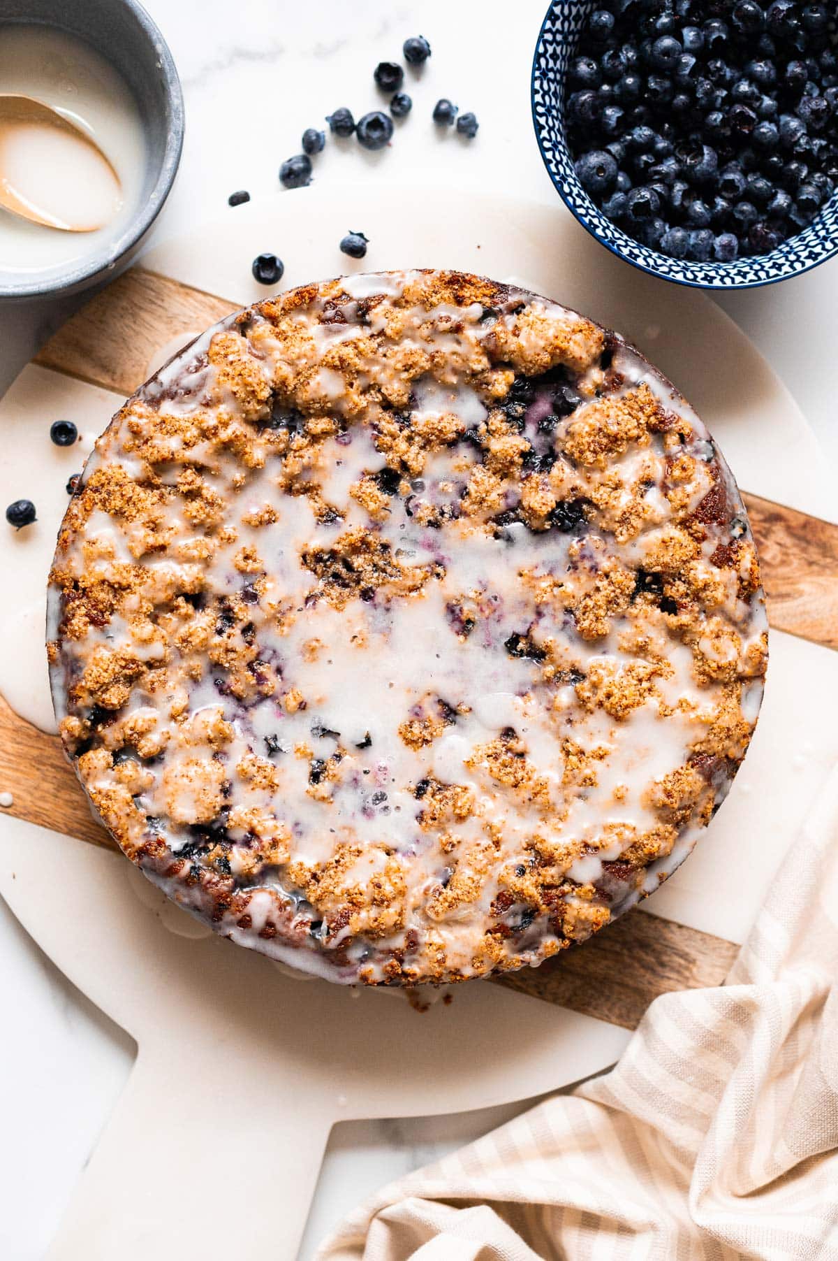 Blueberry coffee cake on a marble board. Fresh blueberries in a bowl and icing glaze on a counter.