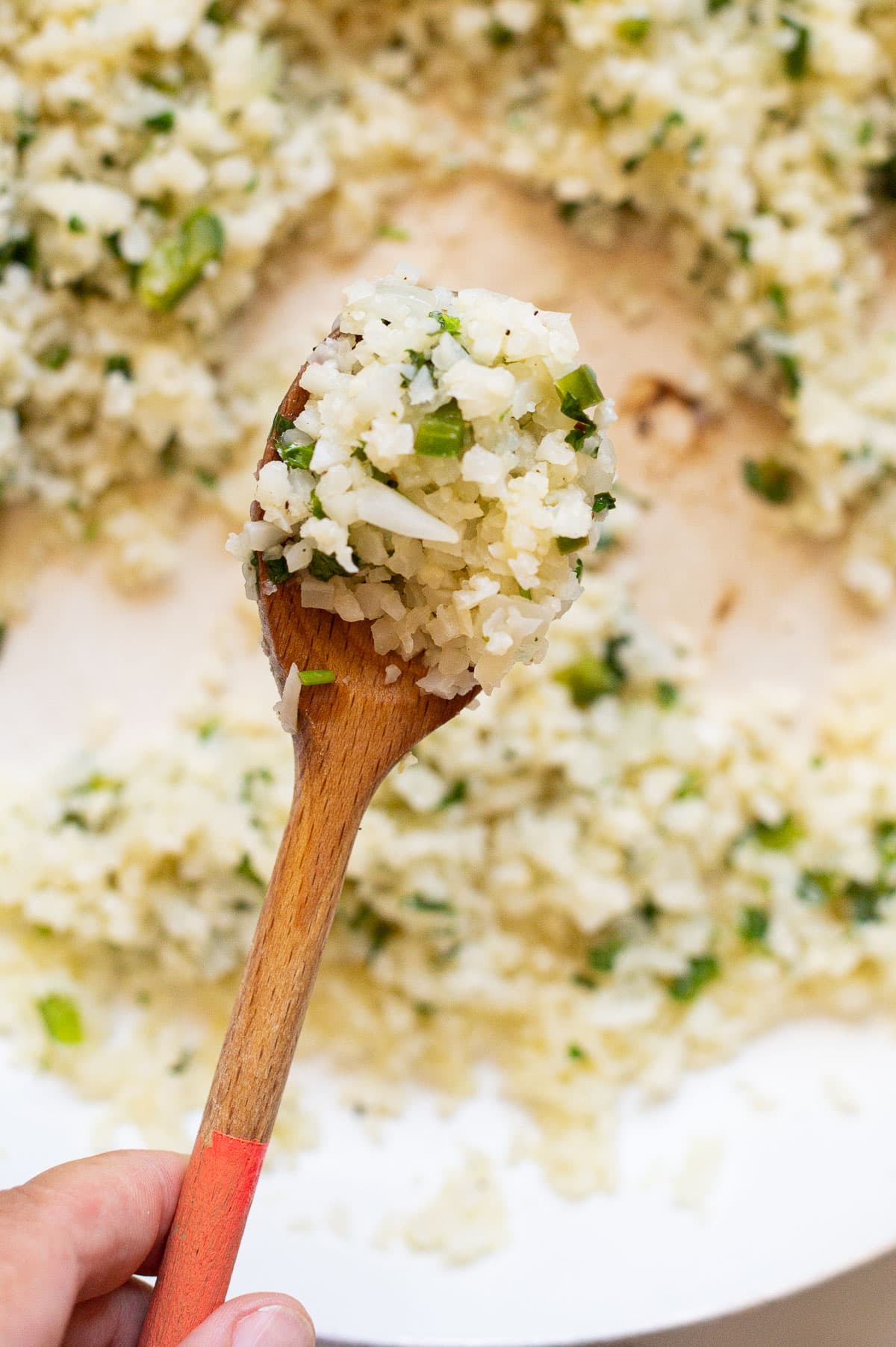Person holding wood spoon with cilantro lime cauliflower rice above the skillet.