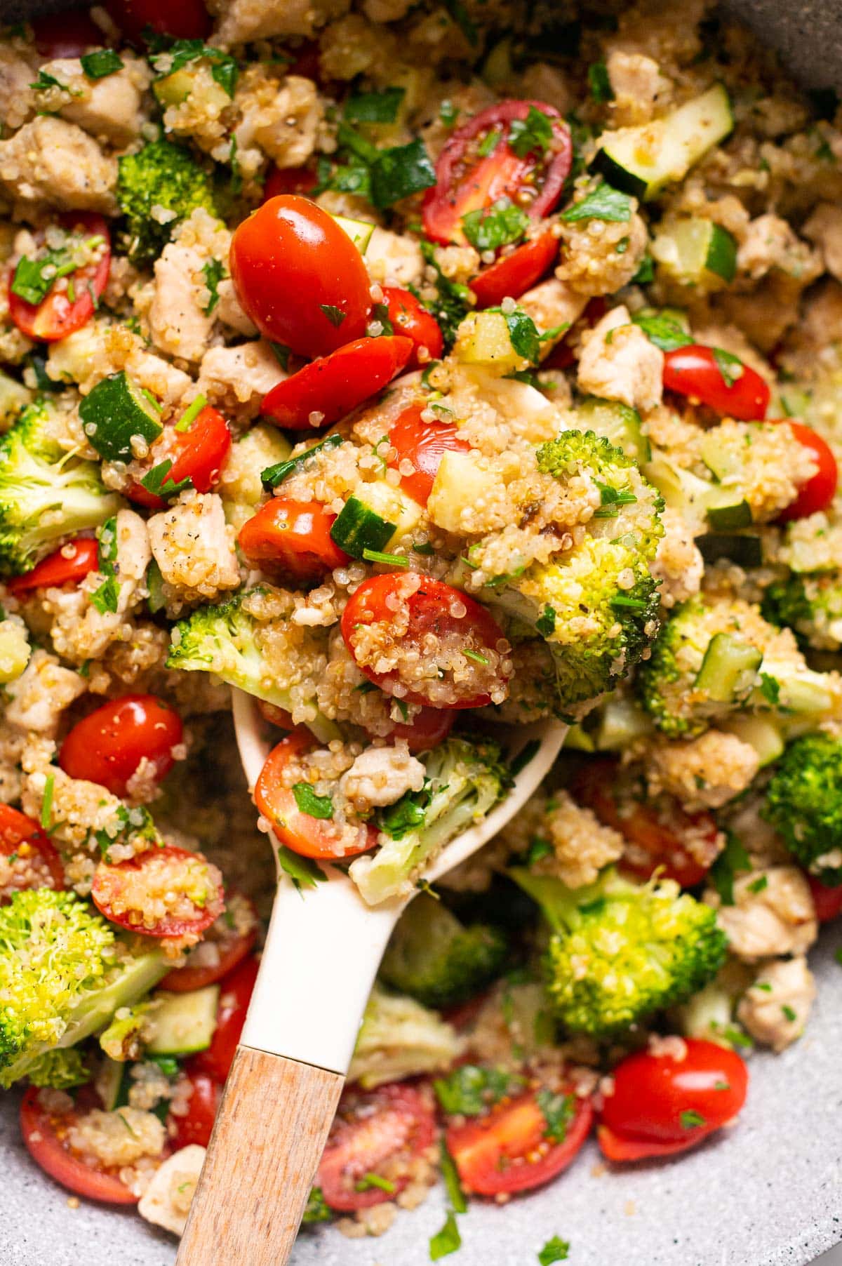 Close up of quinoa skillet with chicken, grape tomatoes, zucchini and broccoli on a spoon.