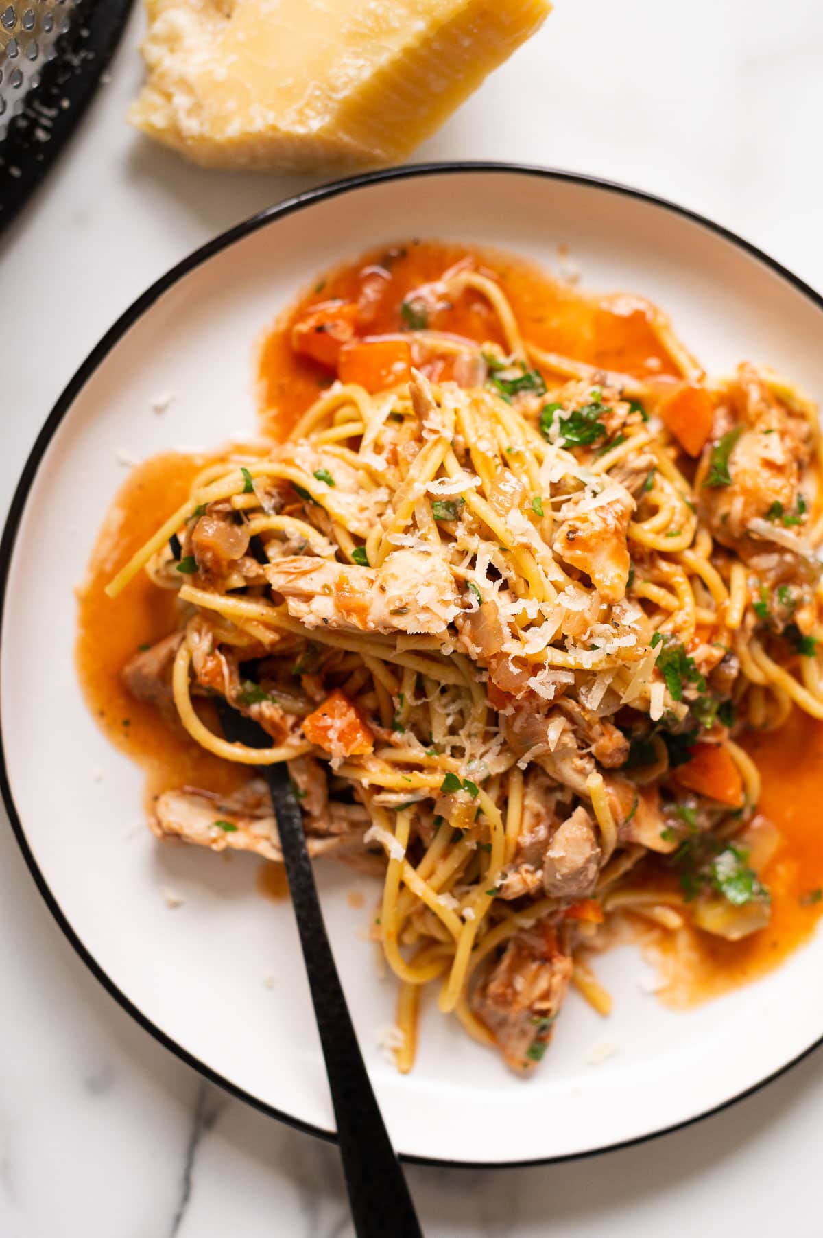 Chicken spaghetti cooked in crock pot and served on a plate garnished with parsley and parmesan cheese.