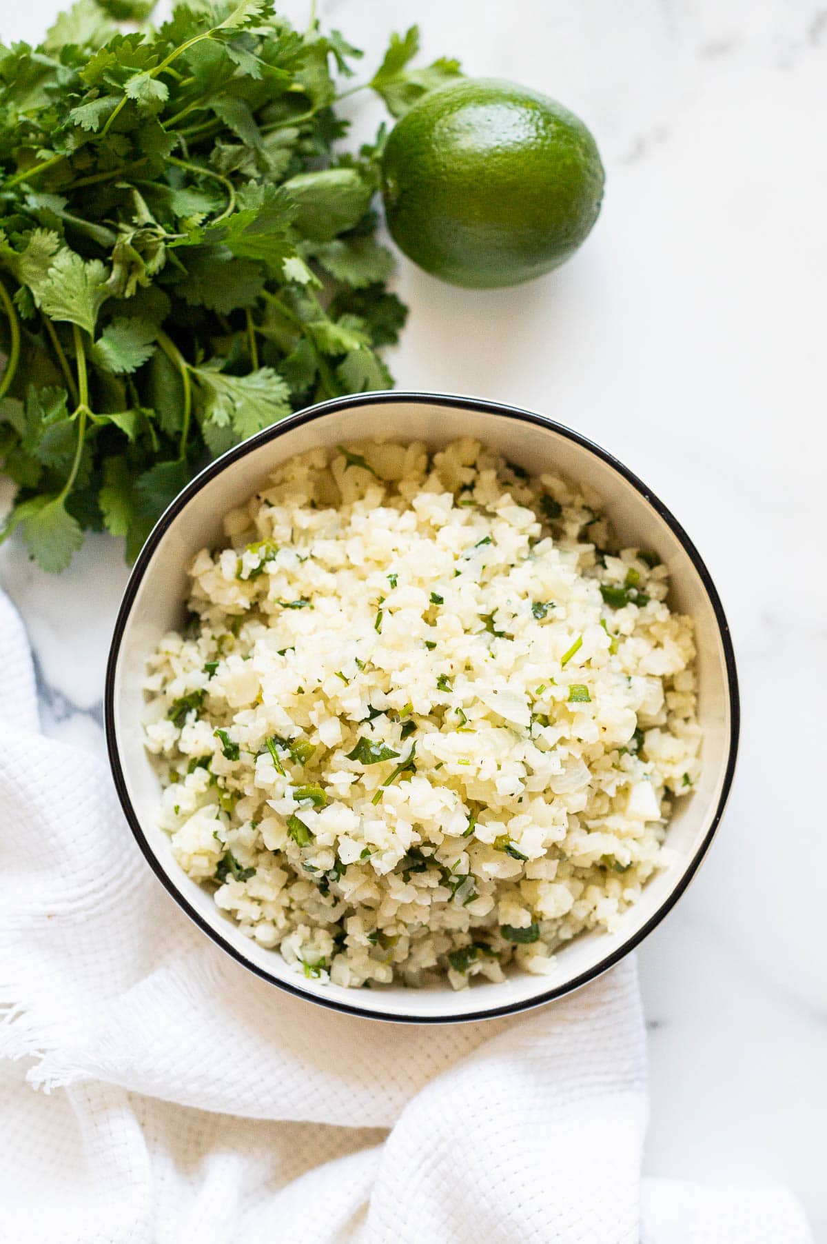 Cilantro lime cauliflower rice served in a bowl. Bunch of cilantro on a counter.