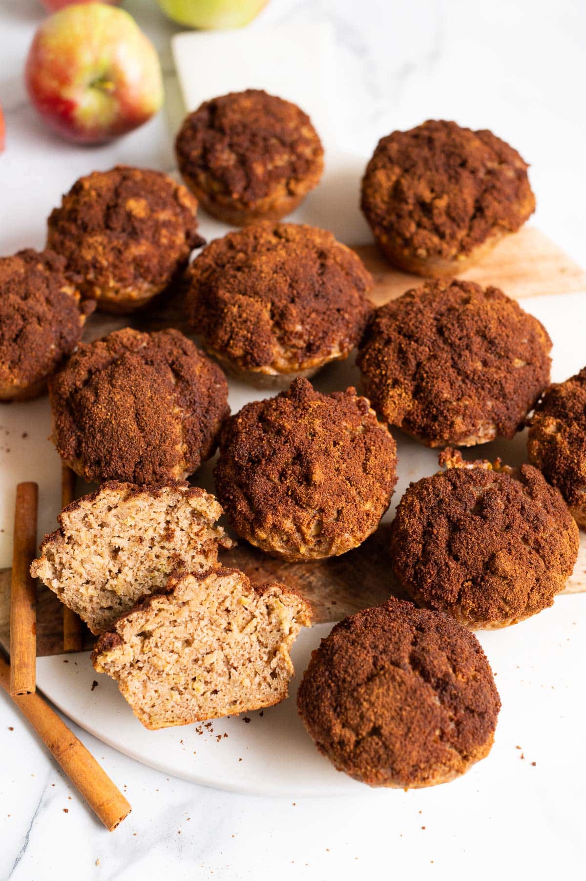 Twelve apple cinnamon muffins on a marble board. One muffin cut in half.