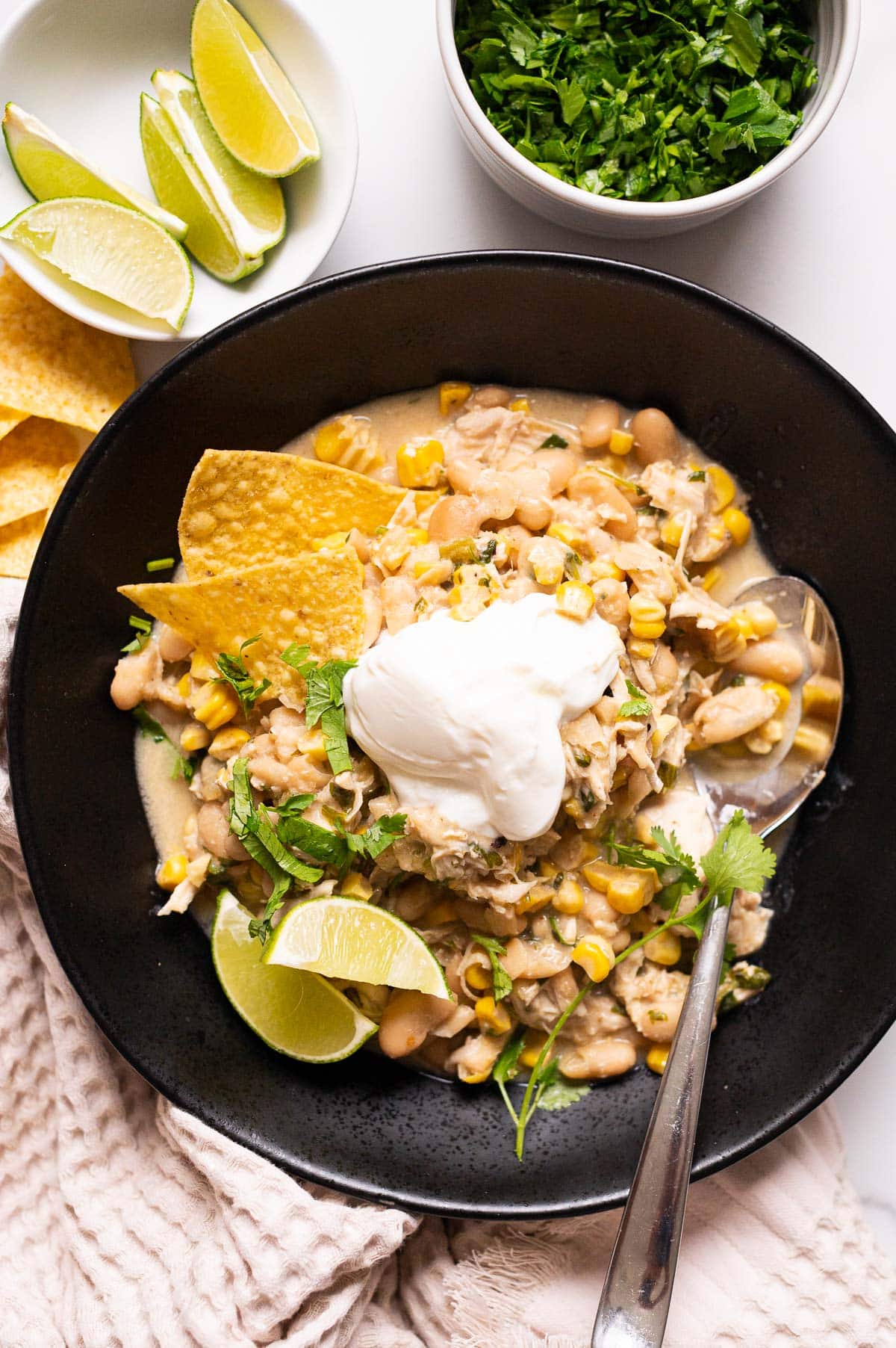 Crockpot white chicken chili served with tortilla chips, sour cream, lime and cilantro in a bowl with a spoon.