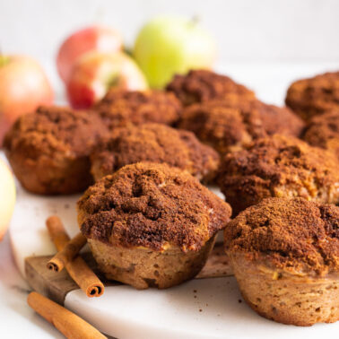 Apple cinnamon muffins on a platter. Cinnamon sticks and apples in the background.