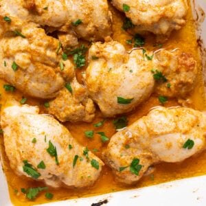 Baked boneless chicken thighs garnished with parsley in a baking dish.