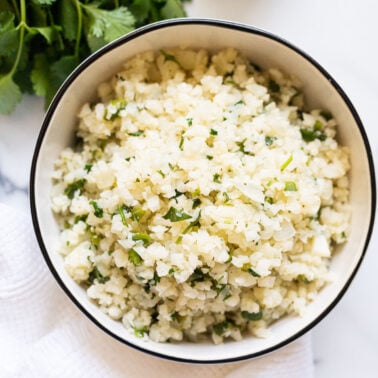 Cilantro lime cauliflower rice served in a bowl. Bunch of cilantro on a counter.