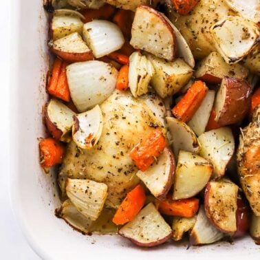 Roasted chicken thighs and potatoes and carrots in white baking dish.