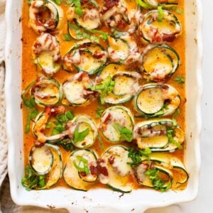 Looking down on zucchini lasagna rolls with sauce in a baking dish.