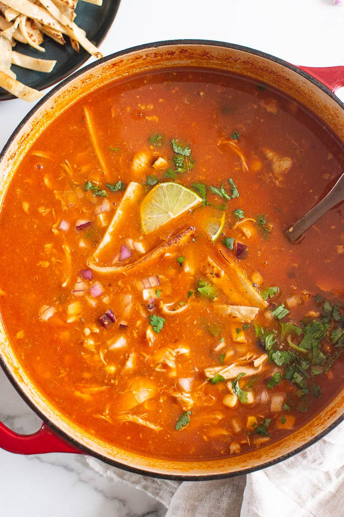 Chicken tortilla soup garnish with lime and cilantro in a pot with ladle.