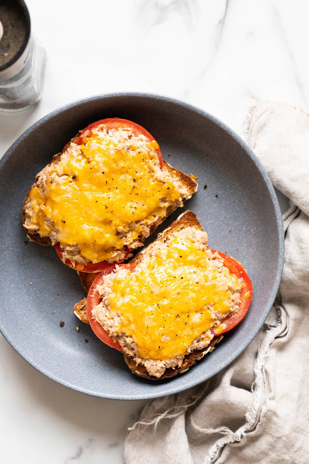 Two healthy tuna melt sandwiches with melted cheese and tomato on blue plate.