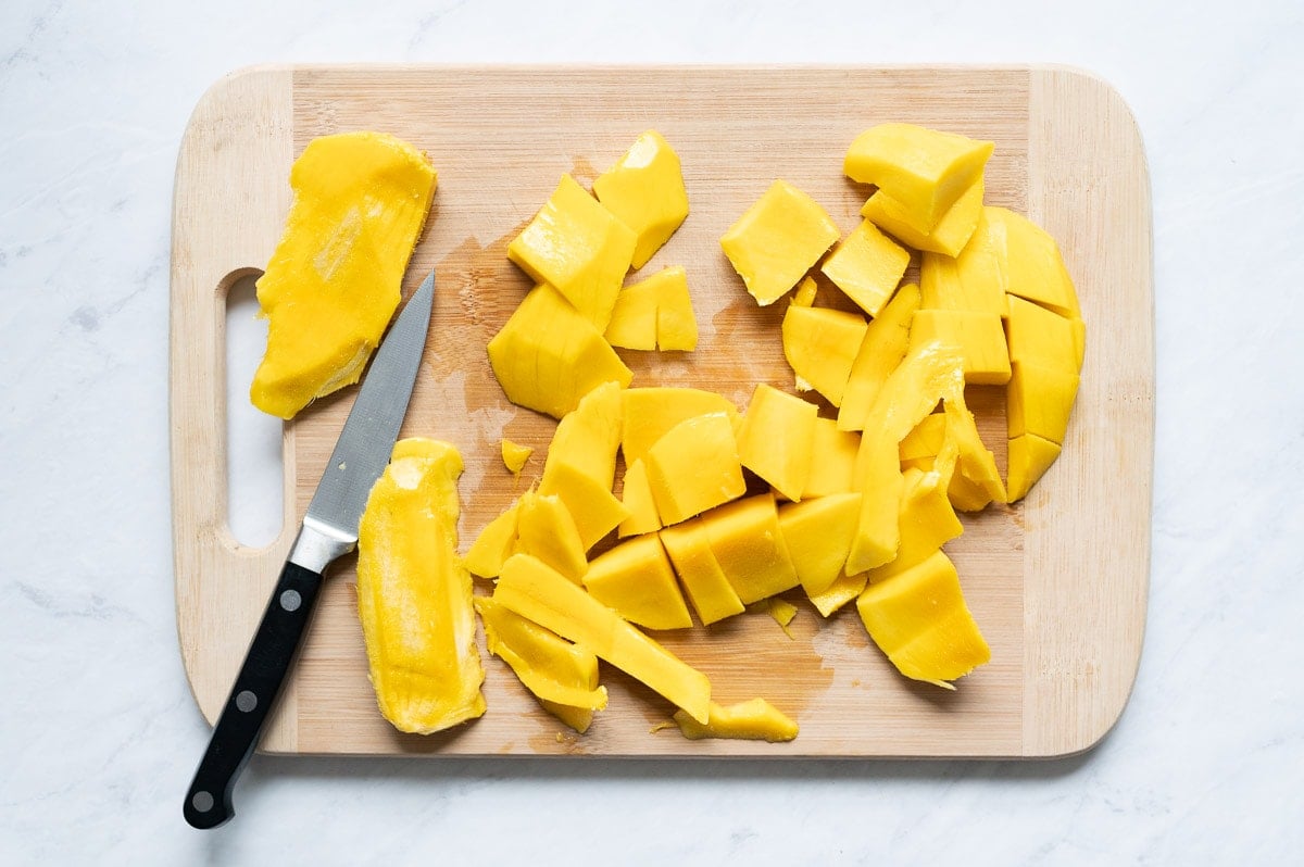 Chopped mango and mango pits on a cutting board with paring knife.