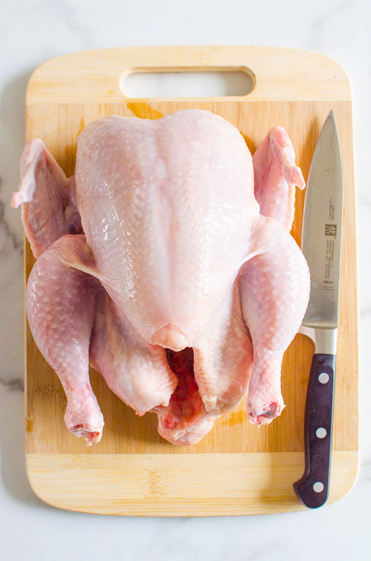 Whole chicken on a cutting board with a knife.
